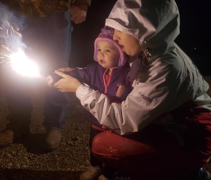 Mother helping her toddler hold a lit sparkler