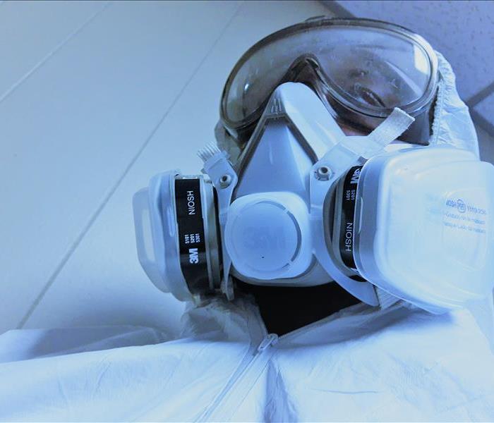 A man in a white protective suit, goggles, respirator and green latex gloves