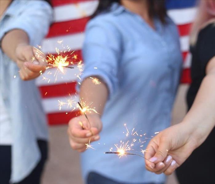 three women hold lit sparklers in their hand away from their bodies