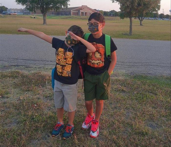 two boys with masks posing for a picture near school