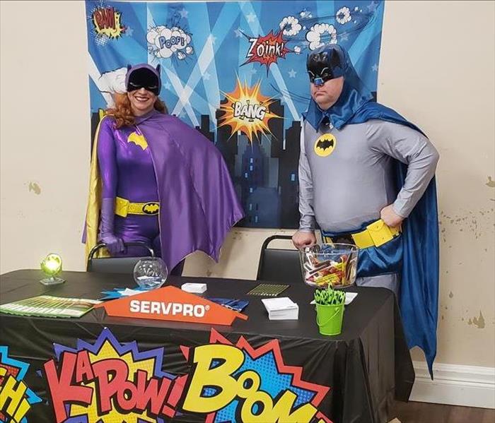 A man dressed as batman and a woman dressed as batgirl at a table decorated with hero items