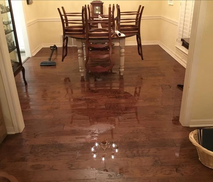 A dining table standing in a puddle in the middle of a wooden floored room