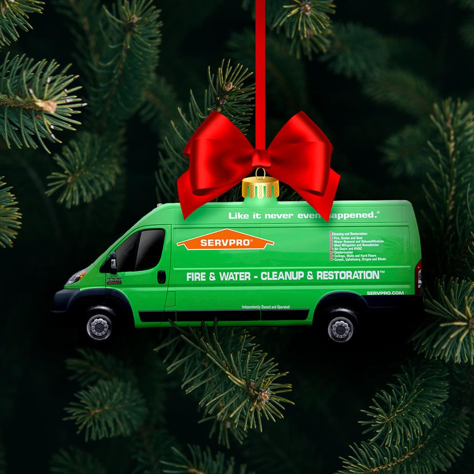 A Christmas tree in the background, a green delivery truck ornament is hanging by a red ribbon